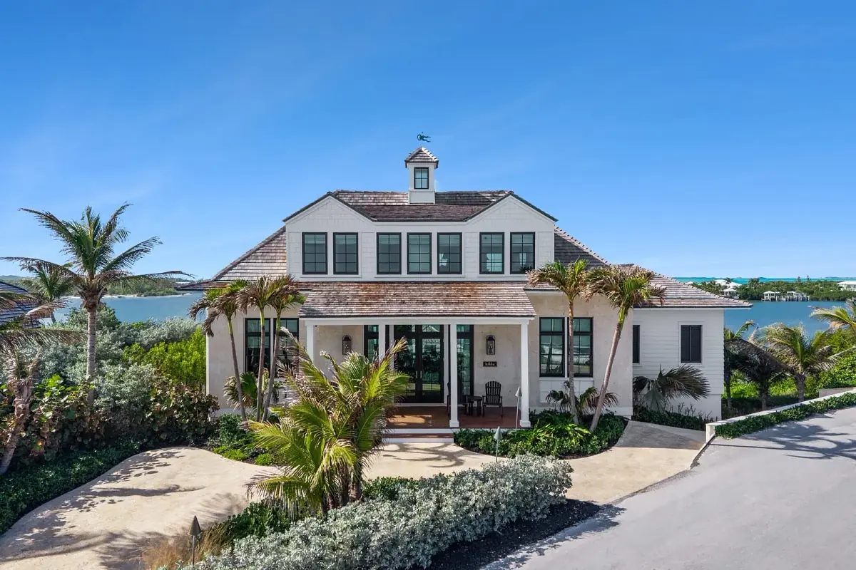 Front exterior of a house with large windows, central entrance, palm trees, and concrete driveway.