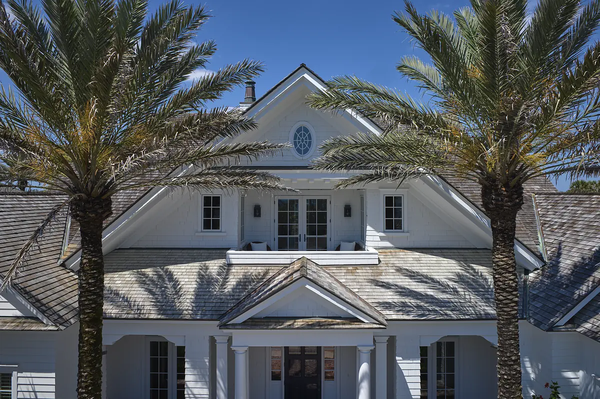 Exterior front view of a house with white siding, gabled roof, palm trees, and double doors with transom.