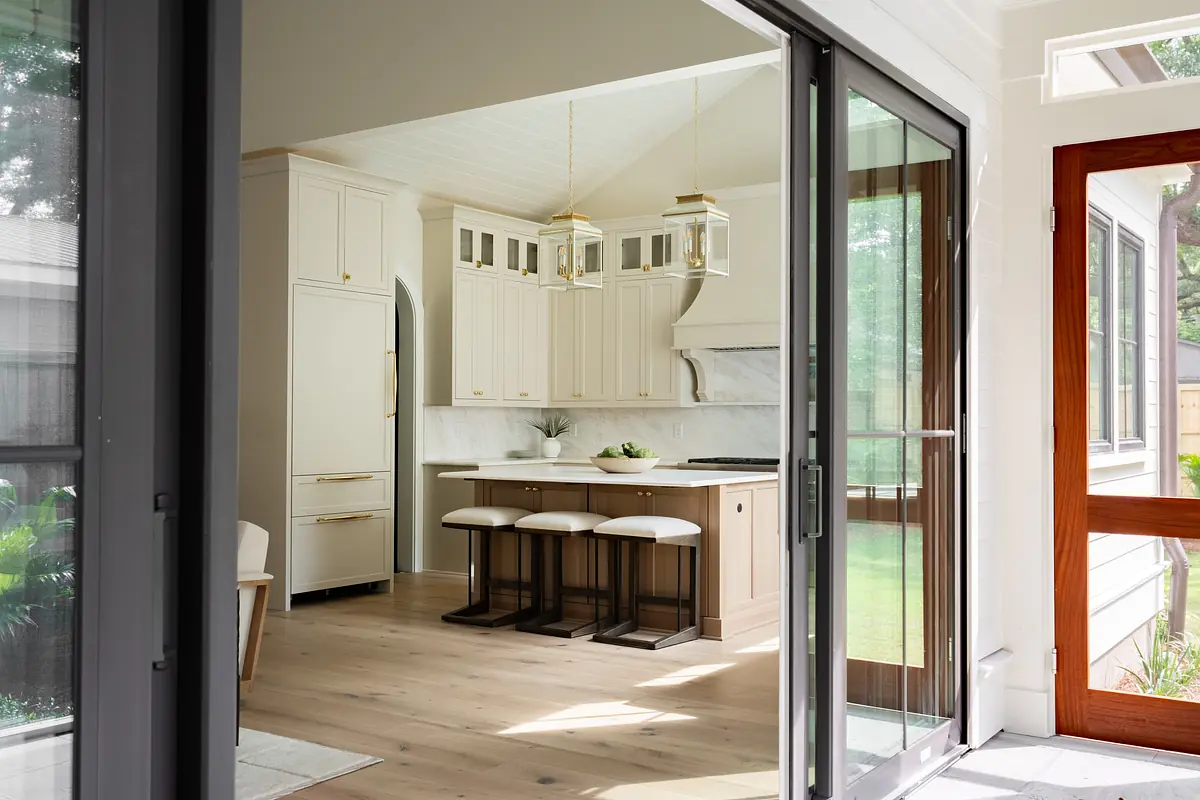 Kitchen with island, bar stools, white cabinetry, marble countertops, and large windows.