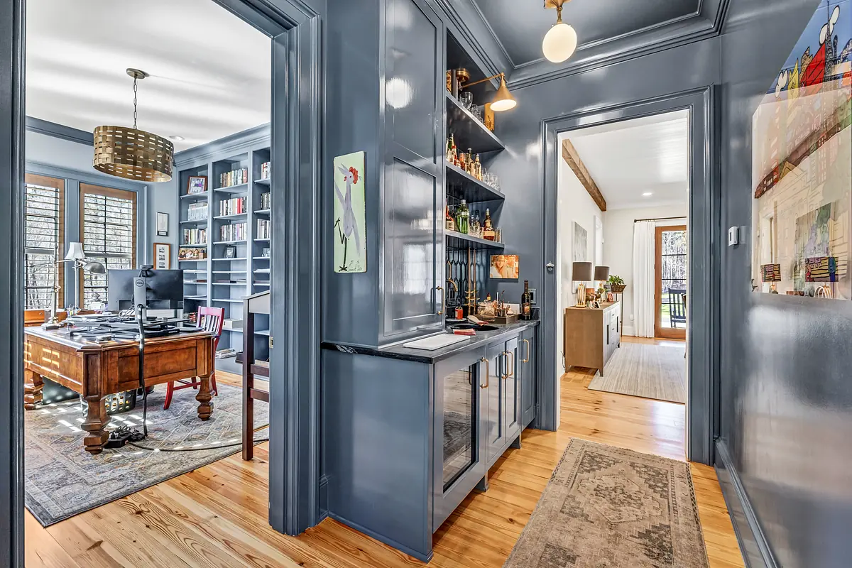Butler's pantry with blue cabinetry, glass shelves, counter, and adjacent room with desk and bookshelves.