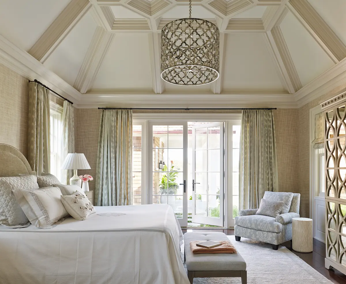 Bedroom with king-size bed, armchair, coffee table, curtains, coffered ceiling, and decorative chandelier
