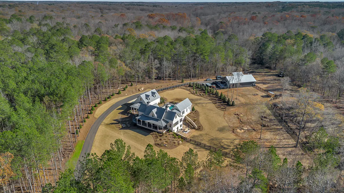 Aerial view of a property with a main house, circular driveway, gardens, and a barn structure.