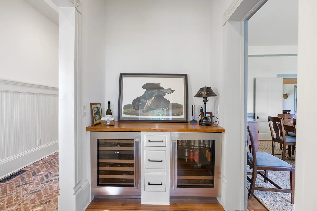 Hallway with wine cooler, wooden countertop, artwork, and decorative lamp leading to a dining area.