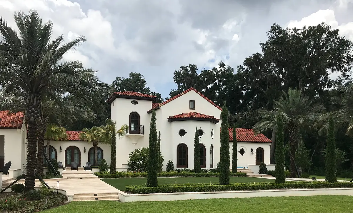 Exterior view of a house with stucco facade, red tile roof, windows, palm trees, and manicured yard.