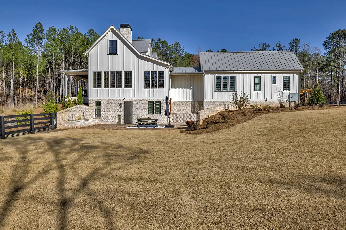 Exterior rear of house with white siding, gray metal roof, large windows, patio, and grassy lawn.