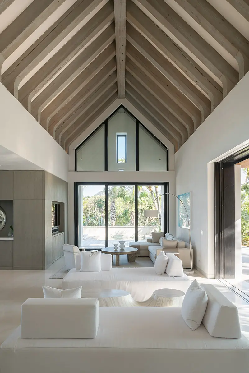 Living room with high ceiling, white sectional sofa, round coffee table, large windows, and views of greenery.