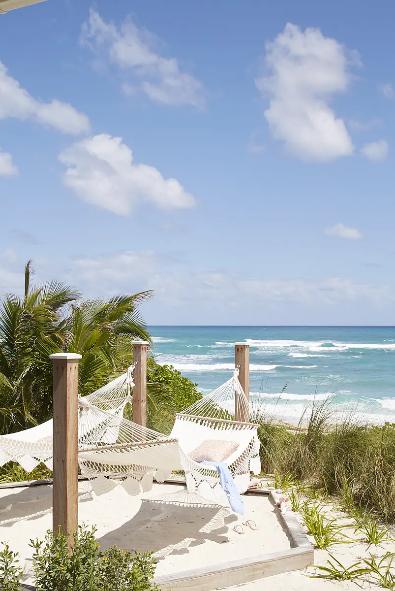 Patio with two white hammocks, sand, greenery, ocean view, and blue sky.