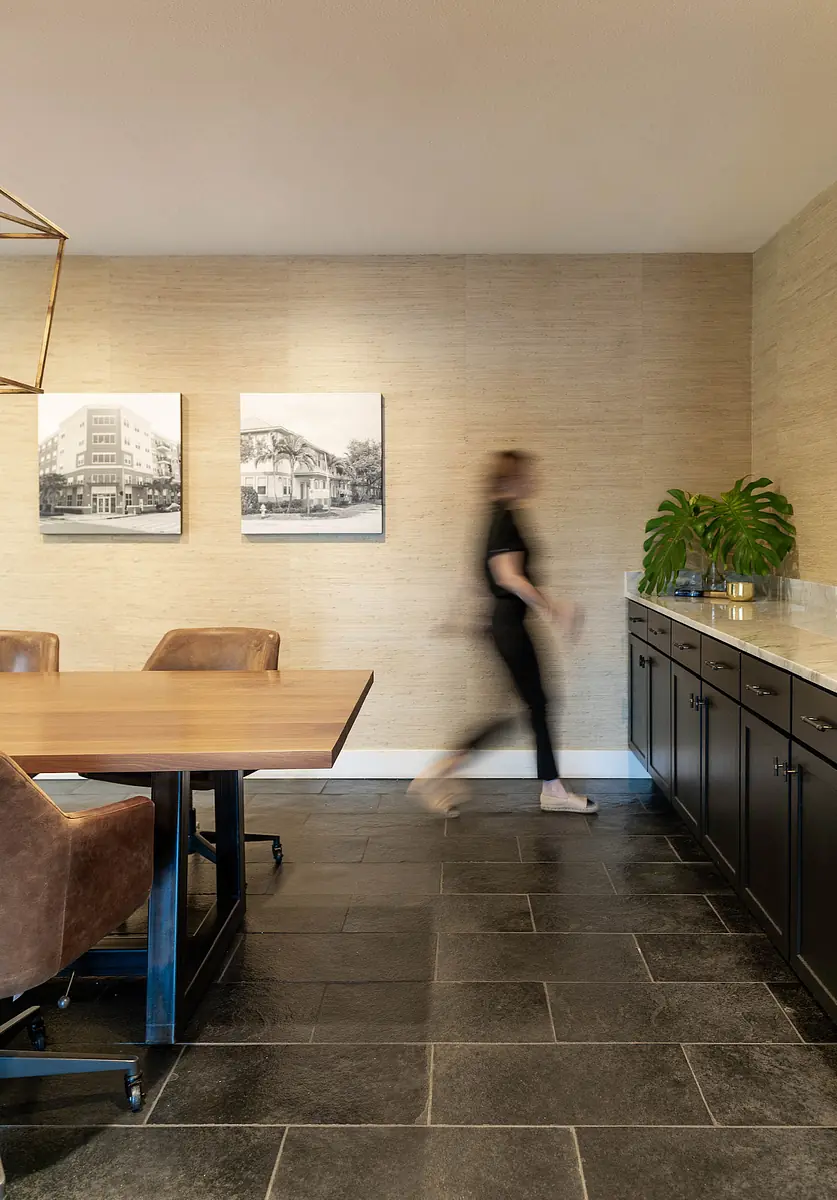 Office space with wooden table, brown chairs, framed photos, green plant, and dark stone floor