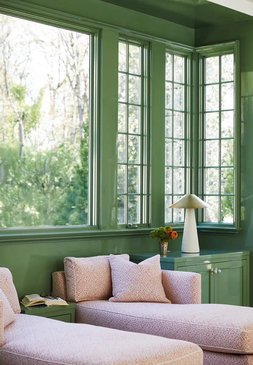 Living room with pink sofas, green chest, white lamp, and large windows providing natural light