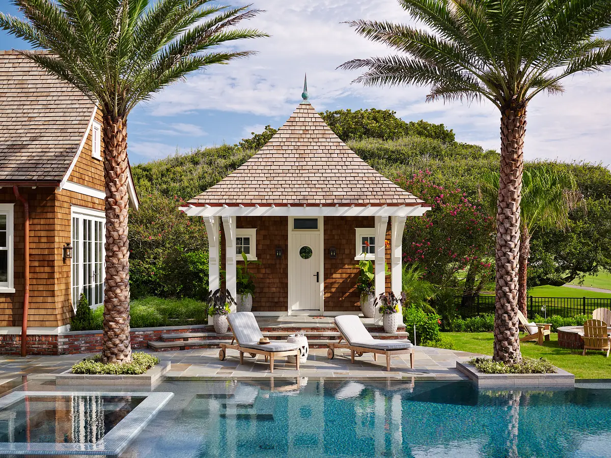 Exterior area with stone patio, swimming pool, lounge chairs, palm trees, and a gazebo with a shingled roof.