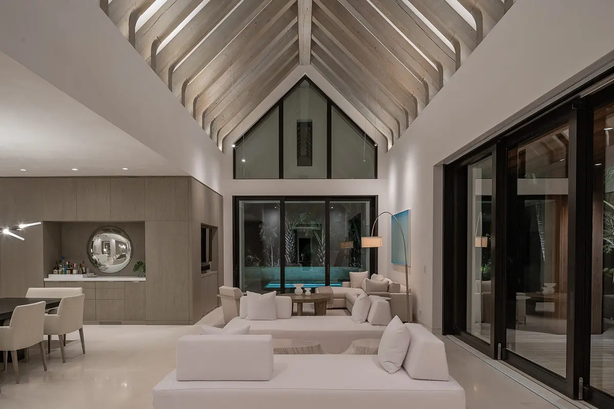 Living room with sectional sofa, coffee table, dining table, large glass doors, and exposed wooden beams