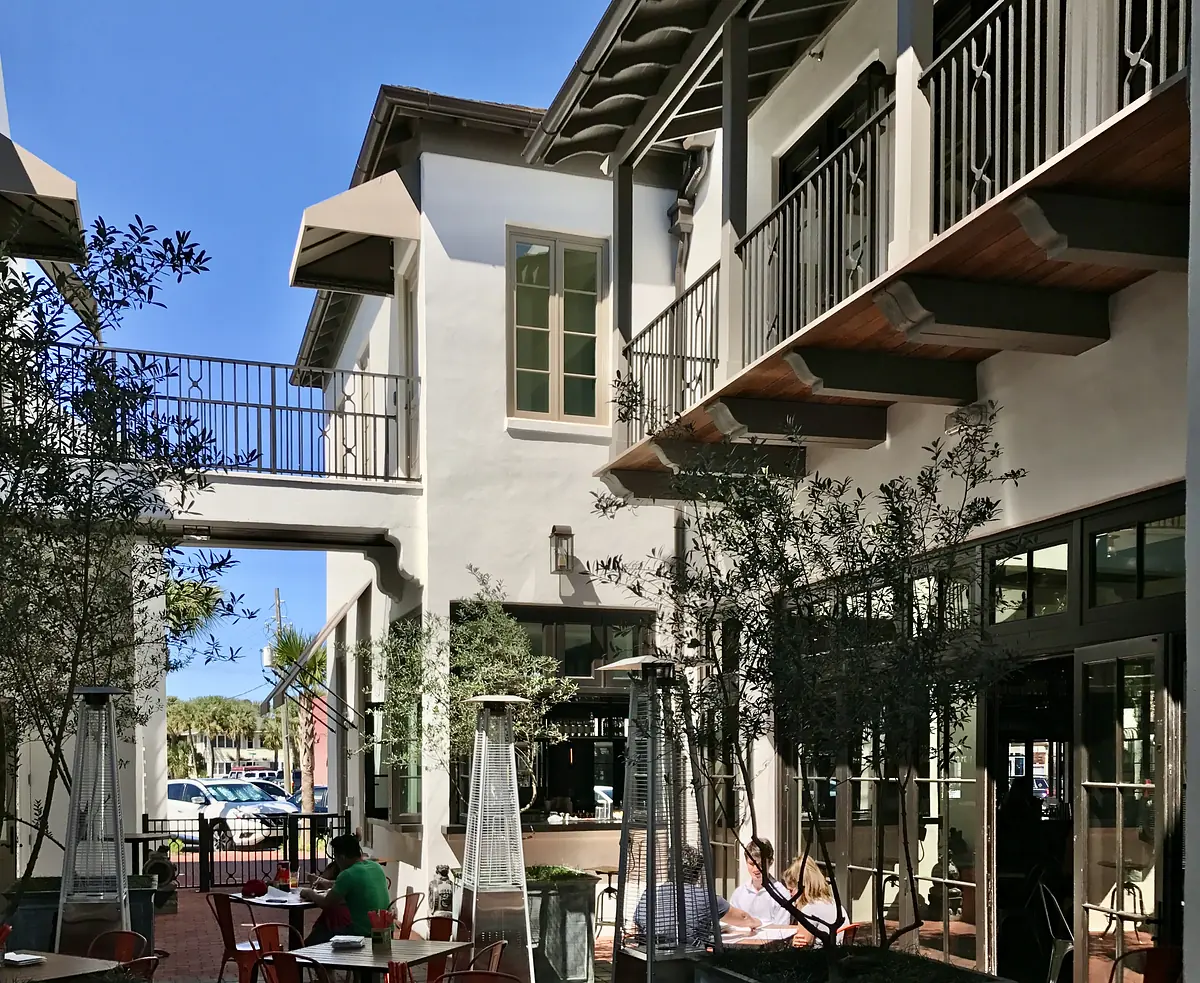 Patio area with metal tables, greenery, glass doors, and a wooden balcony.