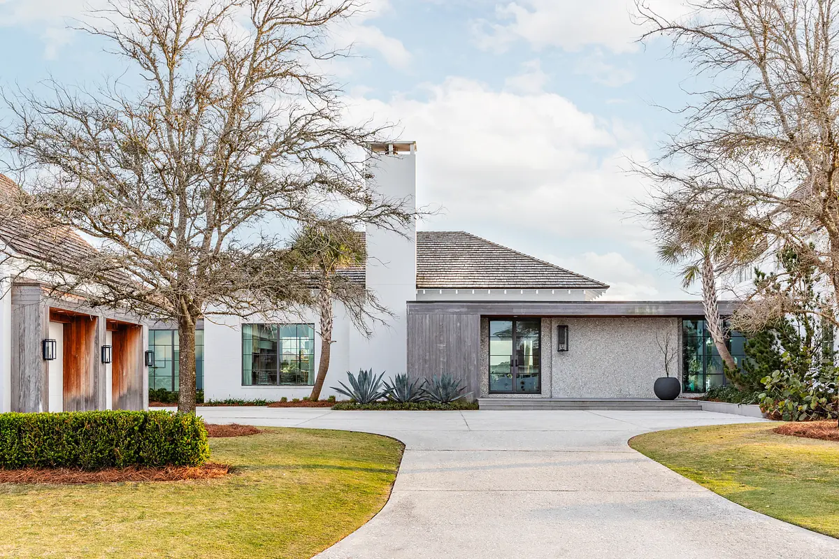 Exterior front view of a house with white stucco, wood paneling, sloped roof, and landscaped driveway.