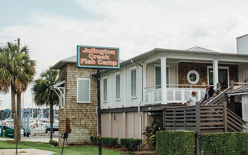 Exterior front view of Julington Creek Fish Camp with wooden siding, deck, and palm trees.