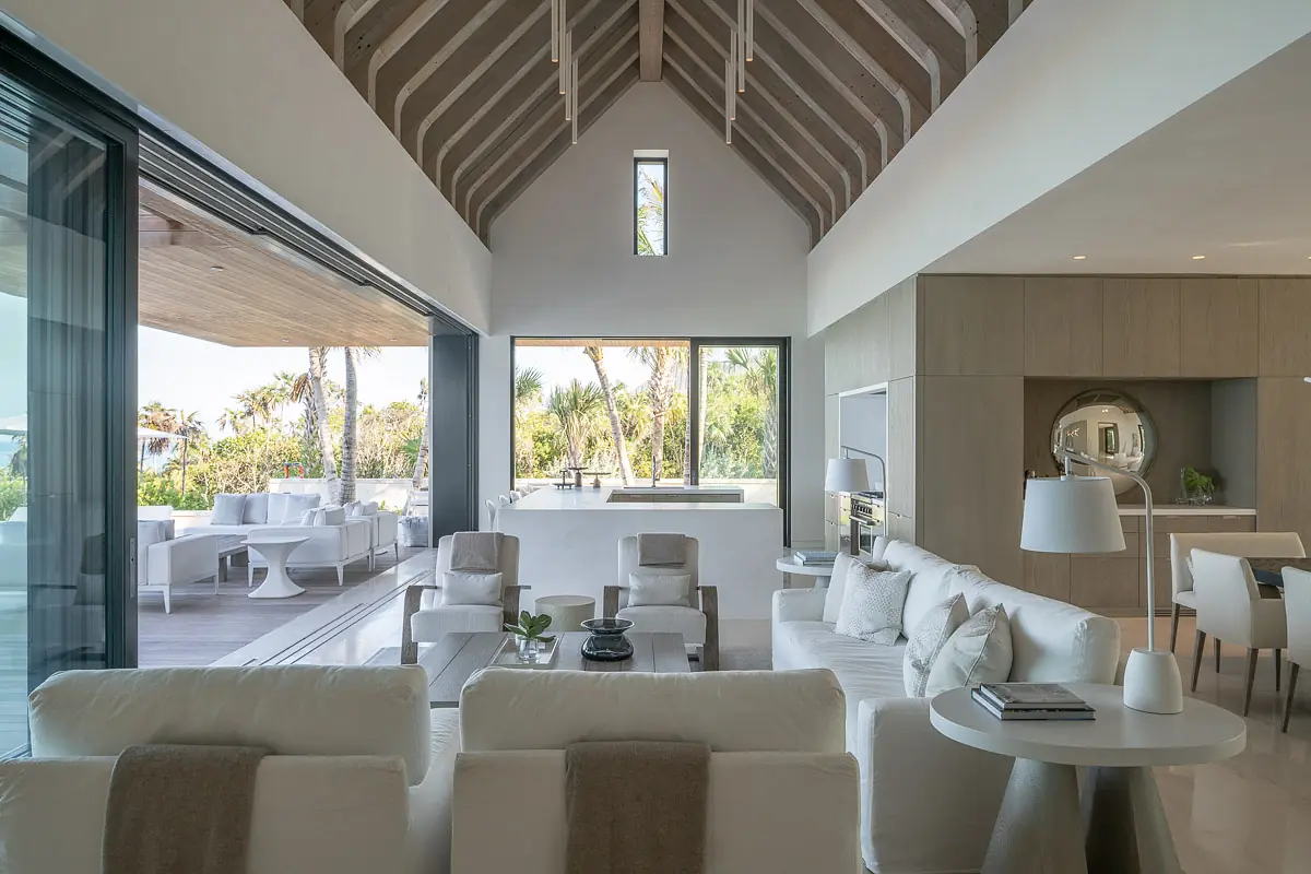 Living room with white sofas, circular coffee table, large windows, wooden beams, and neutral colors.