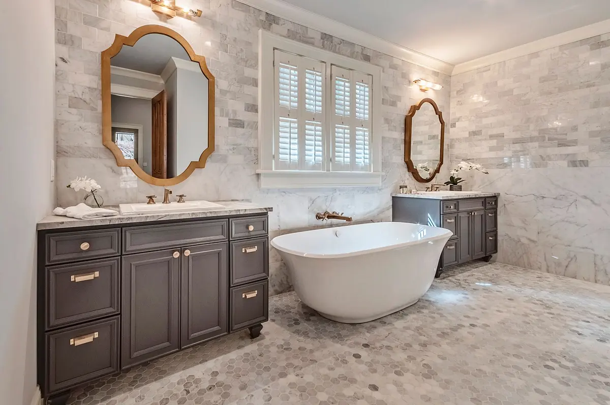 Bathroom with freestanding tub, dark vanities, marble tiles, and plantation shutters on the windows.