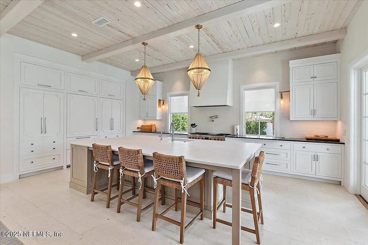 Kitchen with large island, wooden stools, white cabinetry, stainless steel appliances, and exposed beam ceiling