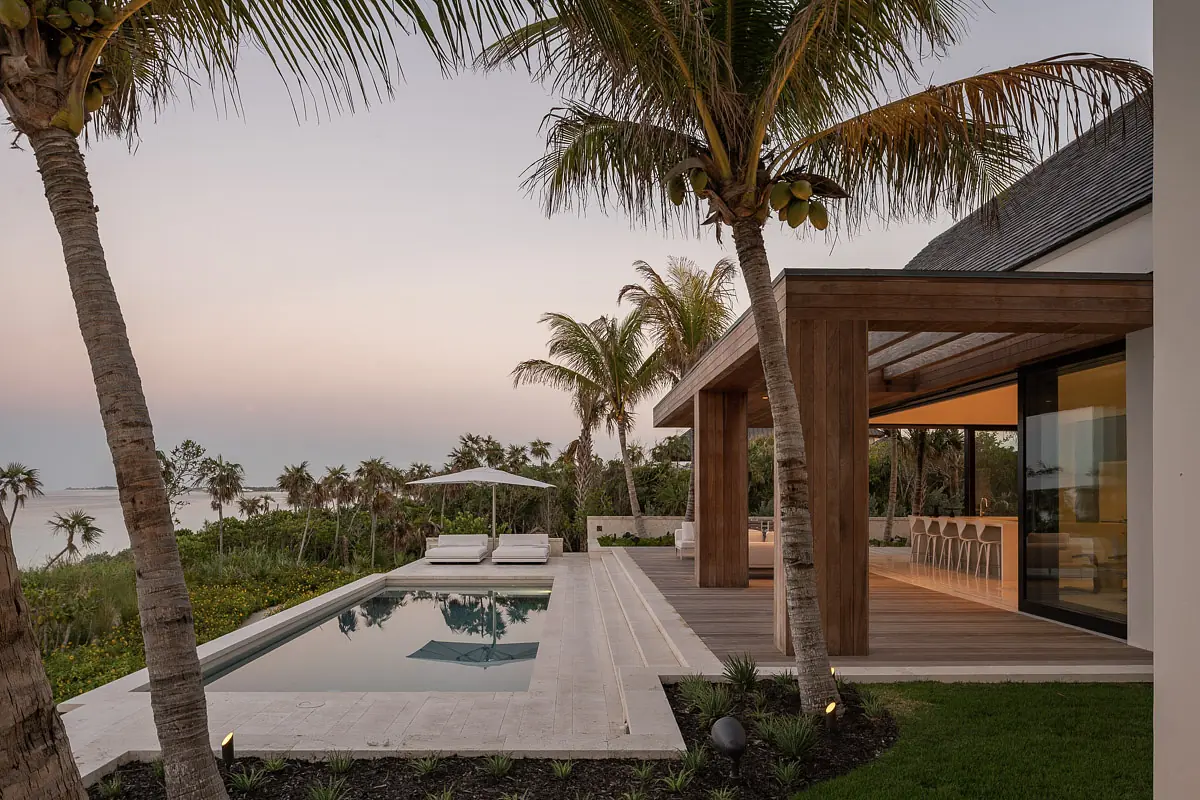 Exterior rear with swimming pool, lounge chairs, covered patio, and palm trees in a landscaped lawn.
