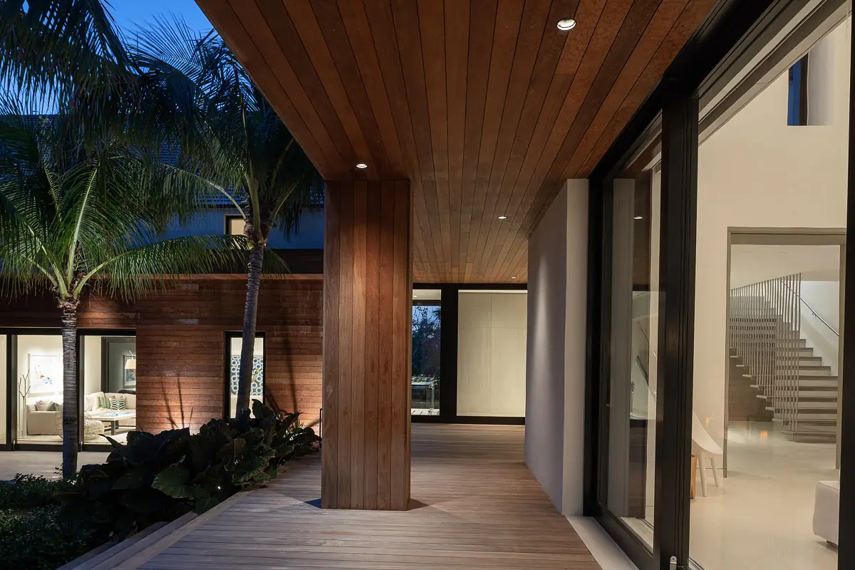 Exterior front with wooden deck, glass windows, palm trees, and recessed lighting.