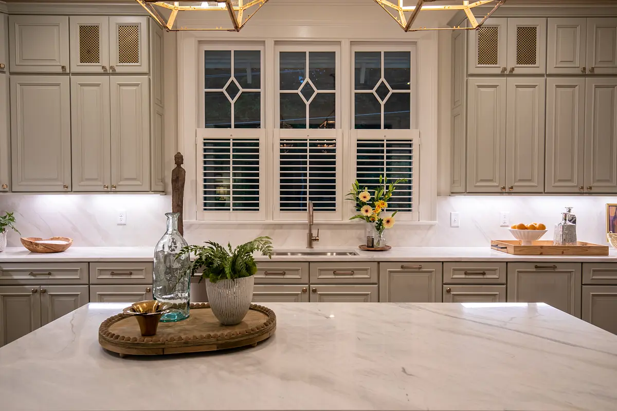 Kitchen with gray cabinetry, marble countertop, large window, decorative tray, vase, and under-cabinet lighting.