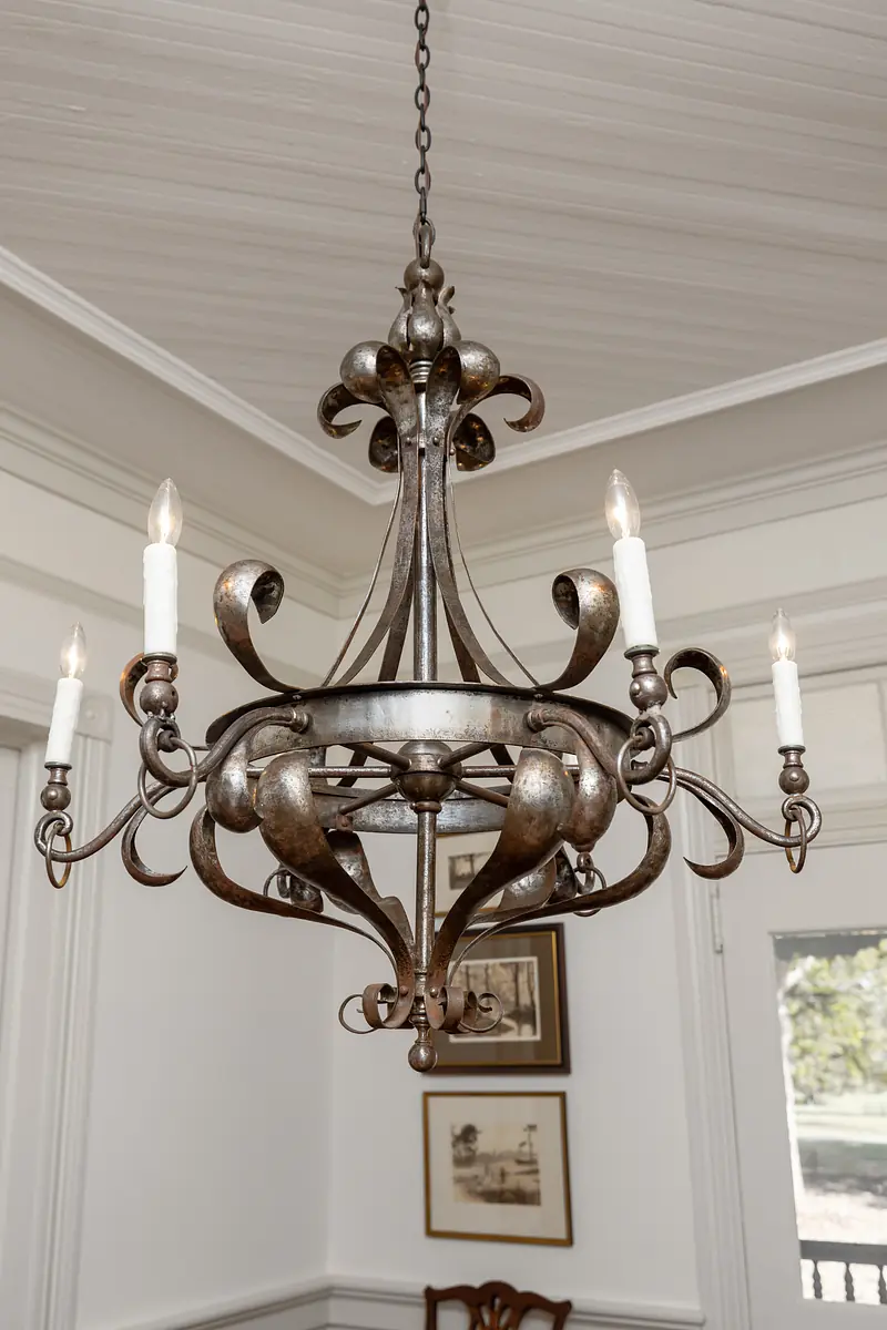 Dining room with wrought iron chandelier, framed artwork, hardwood flooring, and wooden dining table.