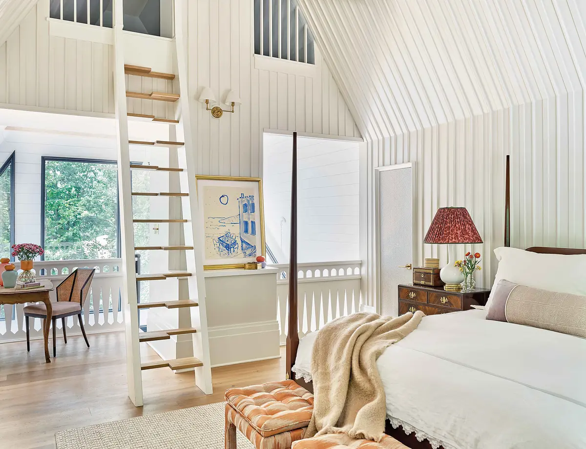 Bedroom with bed, side table, chair, table, ladder, and white paneled walls with large windows
