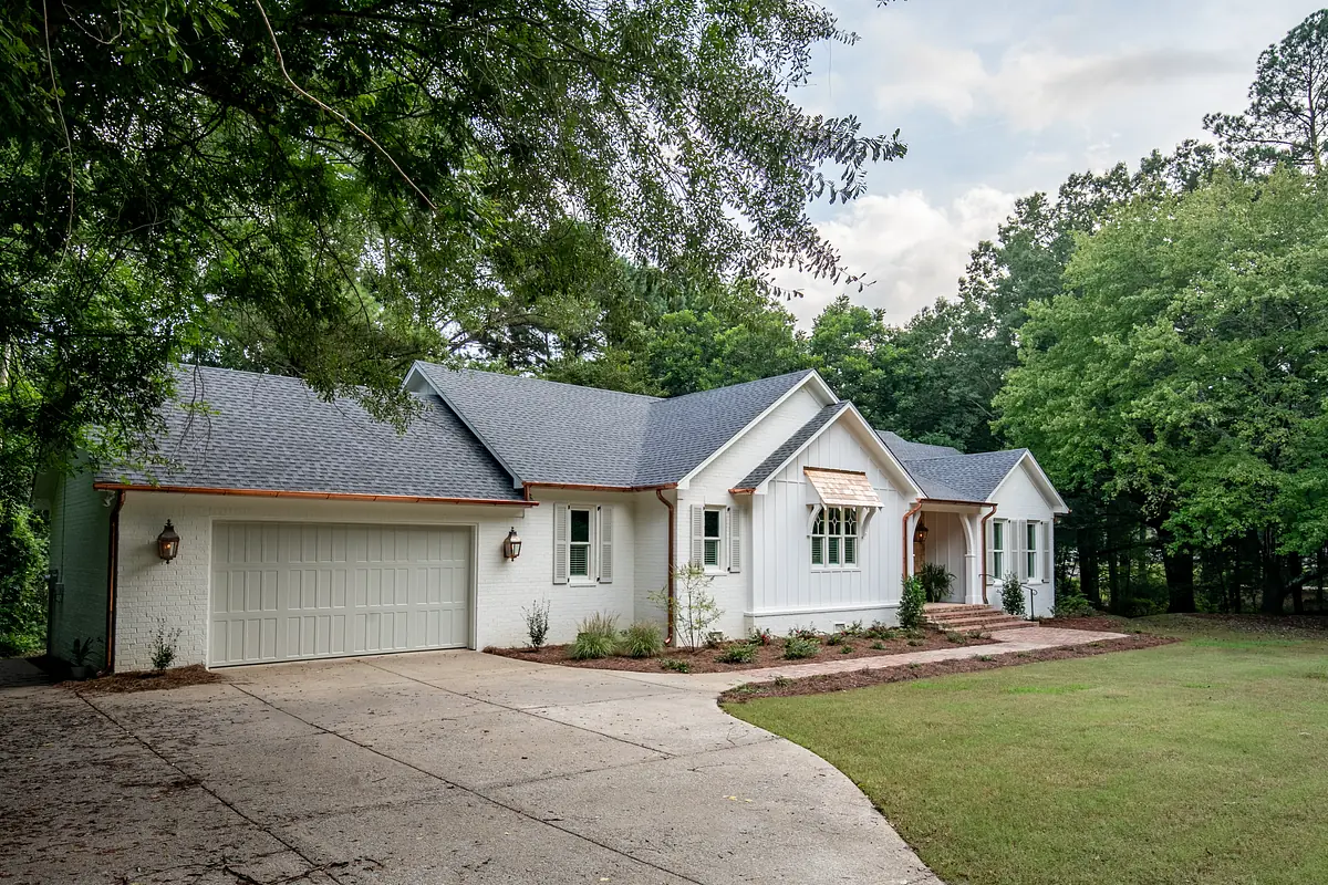 Front exterior of a house with white brick, sloped roof, garage, and landscaping.