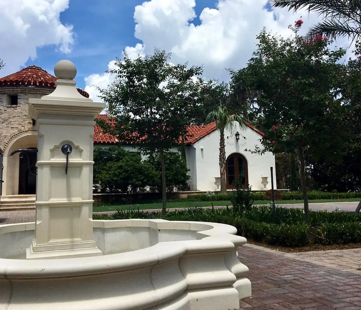 Exterior front with stone fountain, brick paving, terracotta roof, and landscaped greenery.