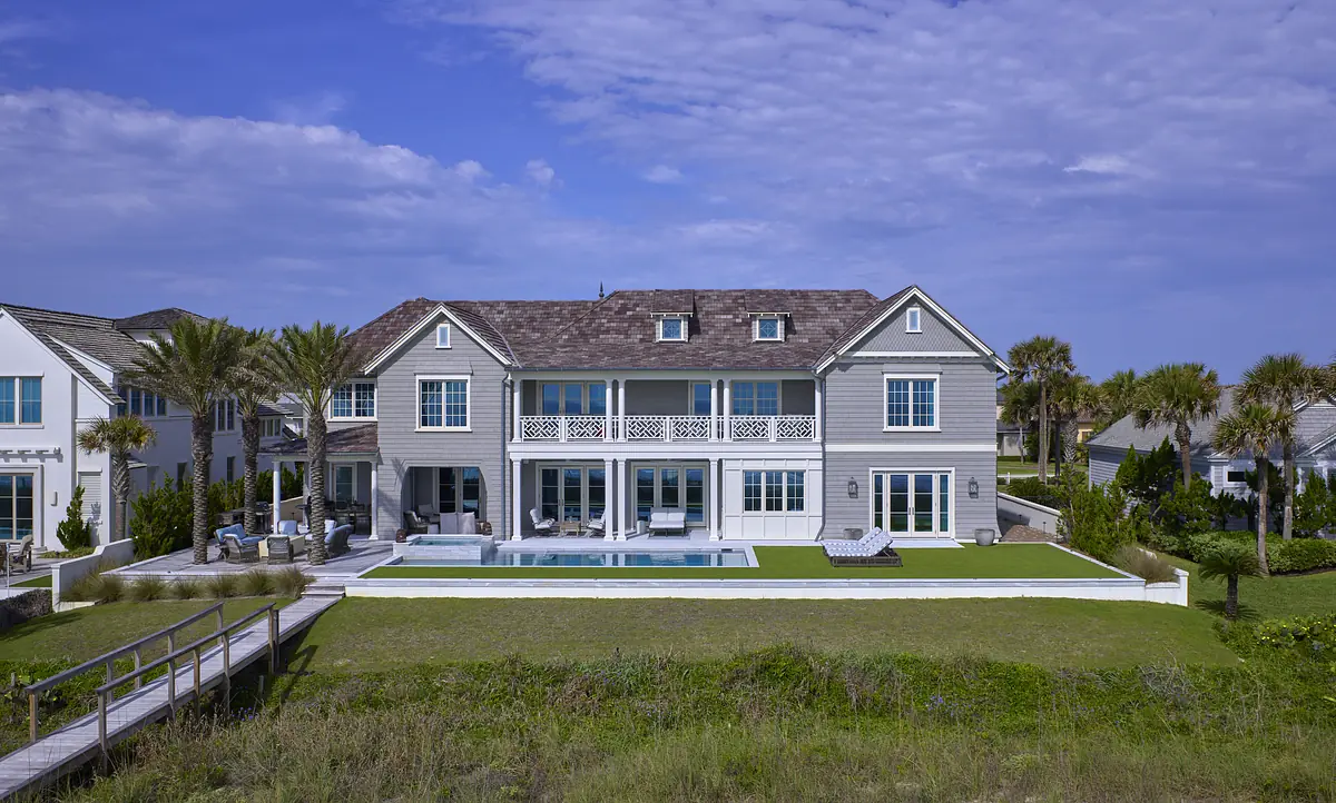 Exterior rear view of a house with gray siding, pool, lounge chairs, and landscaped yard with palms