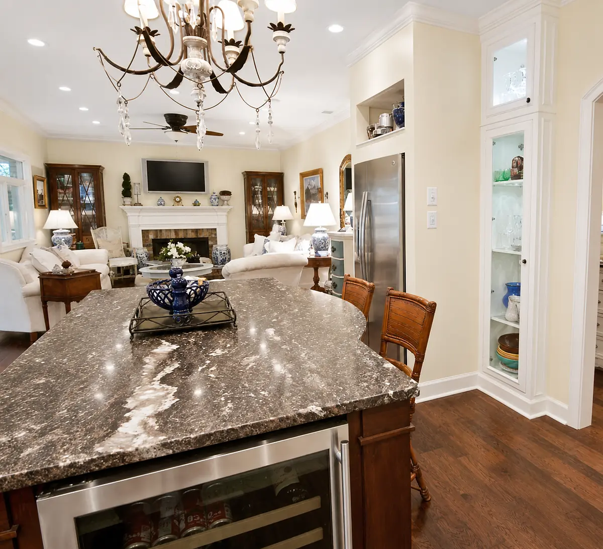 Kitchen with dark granite island, bar stools, stainless steel appliances, and glass-door cabinets.