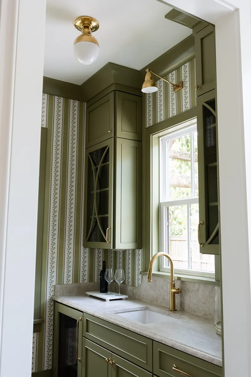 Kitchen with green cabinetry, marble countertop, gold faucet, and window with patterned wallpaper.