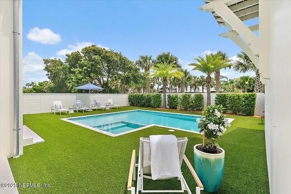 Exterior rear area with swimming pool, grass lawn, lounge chairs, patio umbrella, and palm trees.