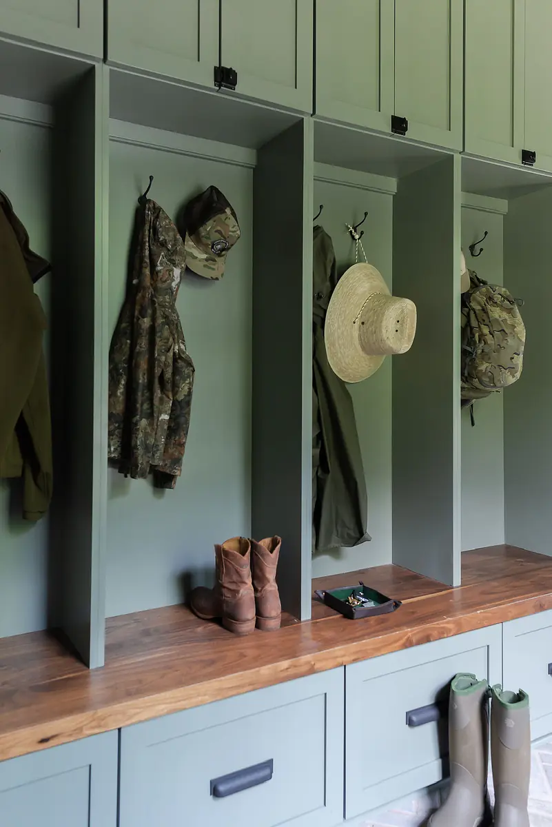 Mudroom with green cubbies, wooden bench, and various coats, hats, and boots.