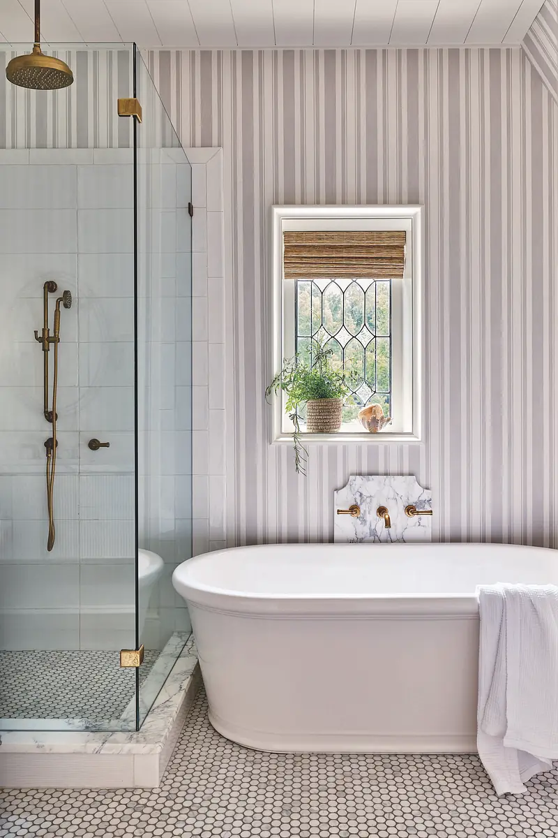 Bathroom with freestanding bathtub, glass shower, mosaic tile floor, and vertical striped wallpaper.