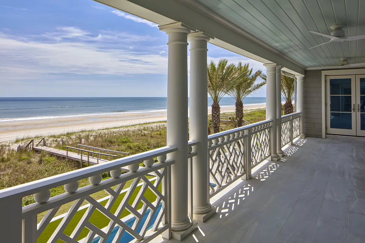 Outdoor deck with white railings, columns, and views of beach and ocean.