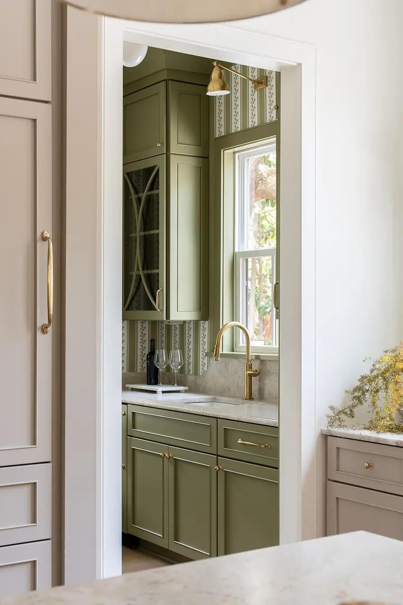 Kitchen with olive green cabinetry, marble countertop, window, and gold faucet.