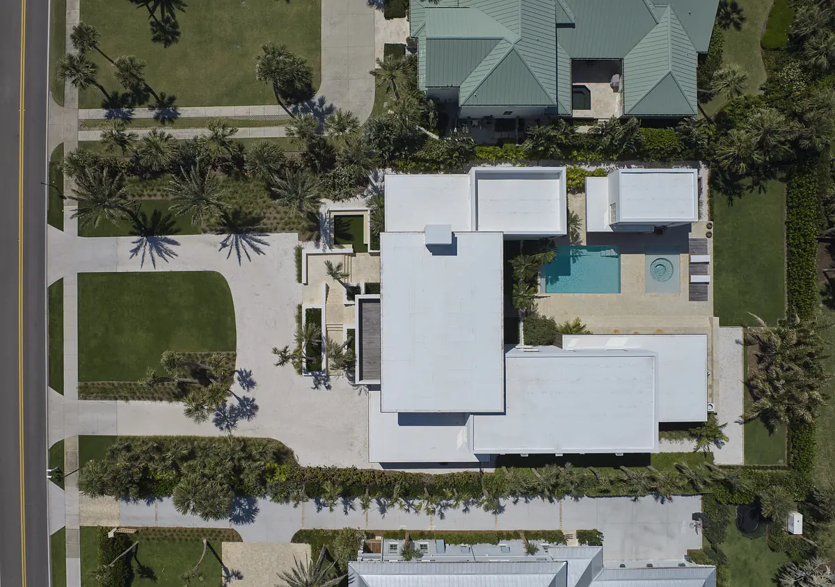Aerial view of a residential property with a pool, patio, green areas, and palm trees.