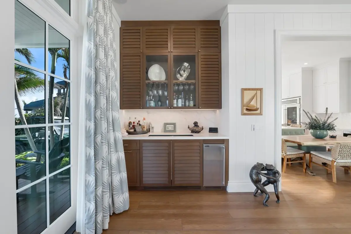 Space with wooden cabinet, glassware, mini refrigerator, patterned curtain, and decorative sculpture