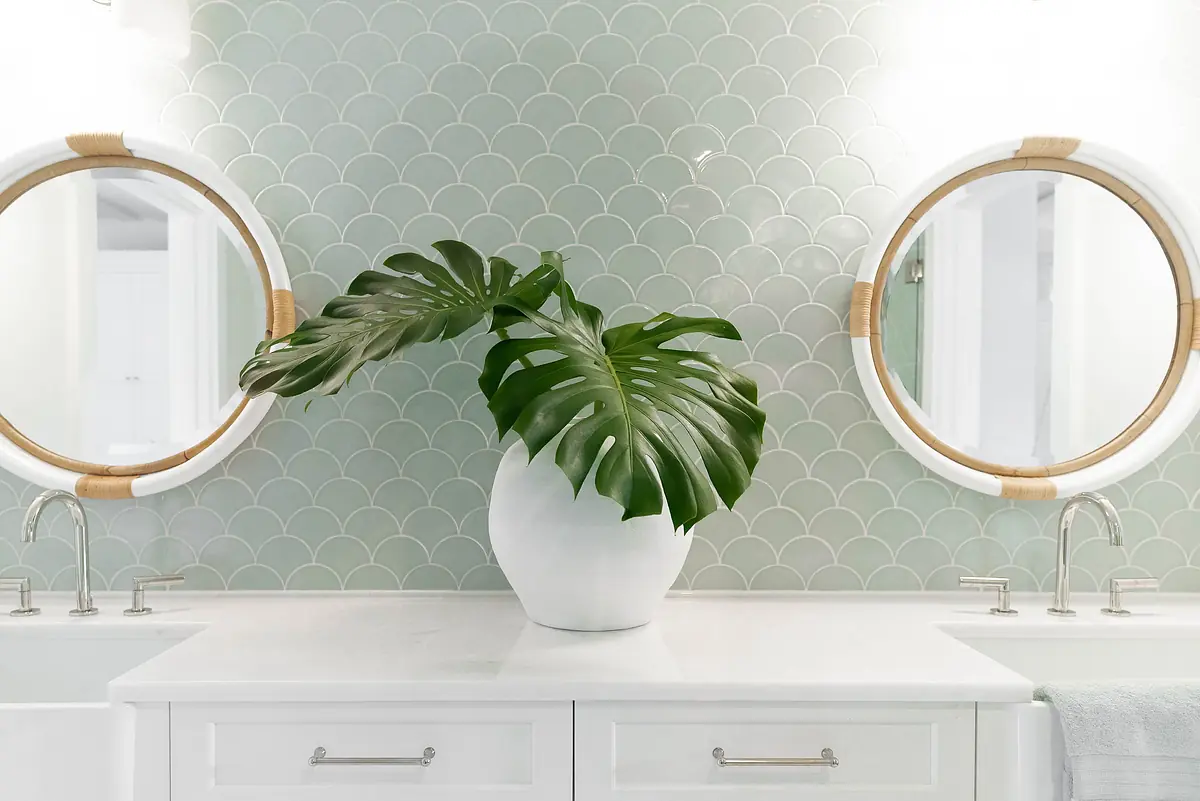 Bathroom with double vanity, round mirrors, green scalloped tiles, and large potted plant.