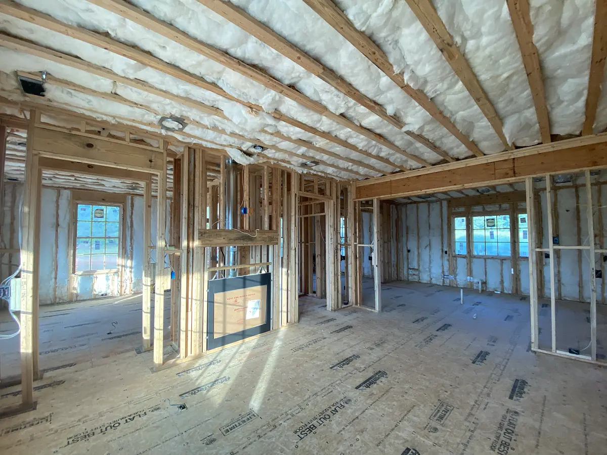 Unfinished construction space with exposed framing, insulation, wooden sheathing, and two windows.