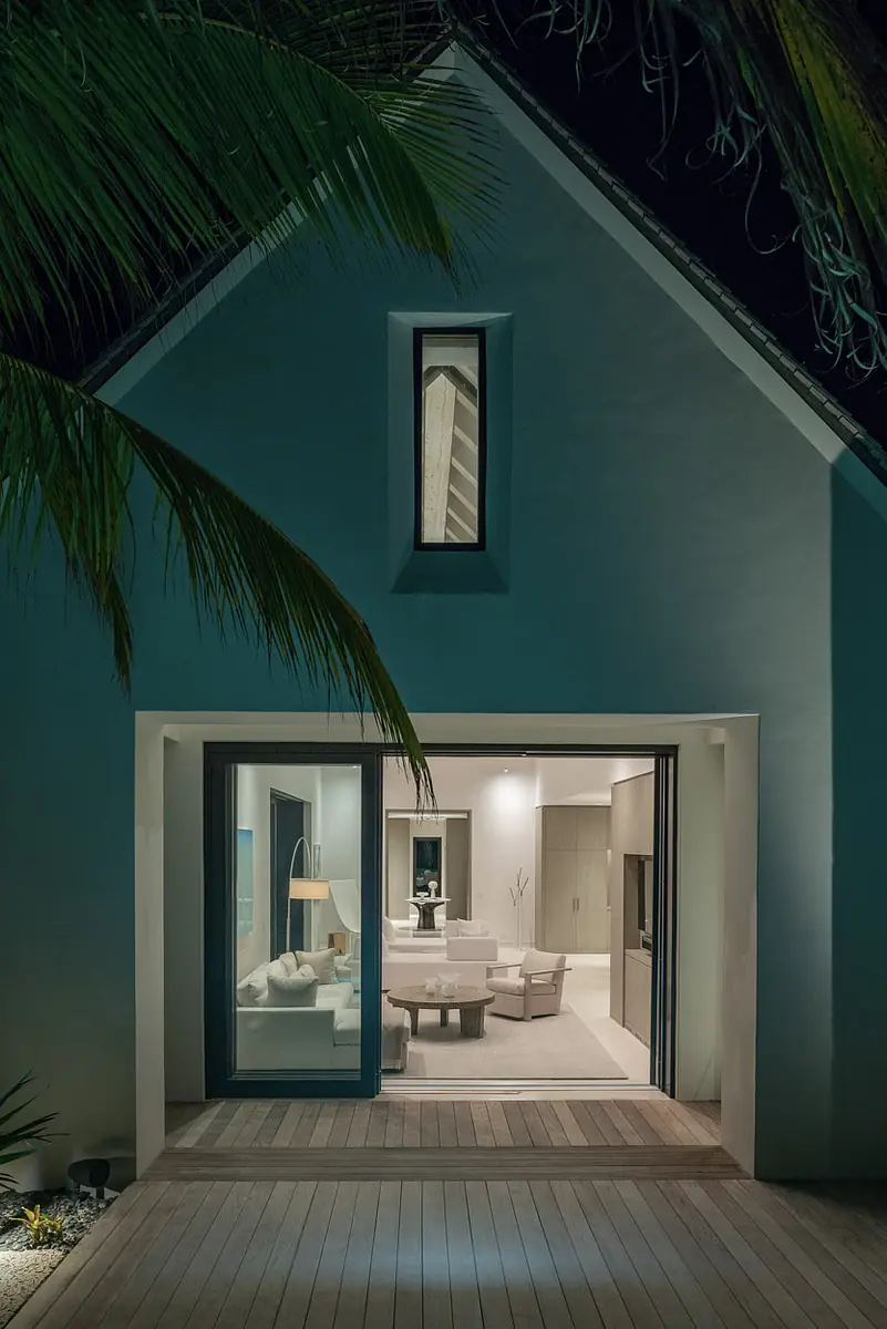 Living room view from outside with white sofas, coffee table, and large sliding glass door.