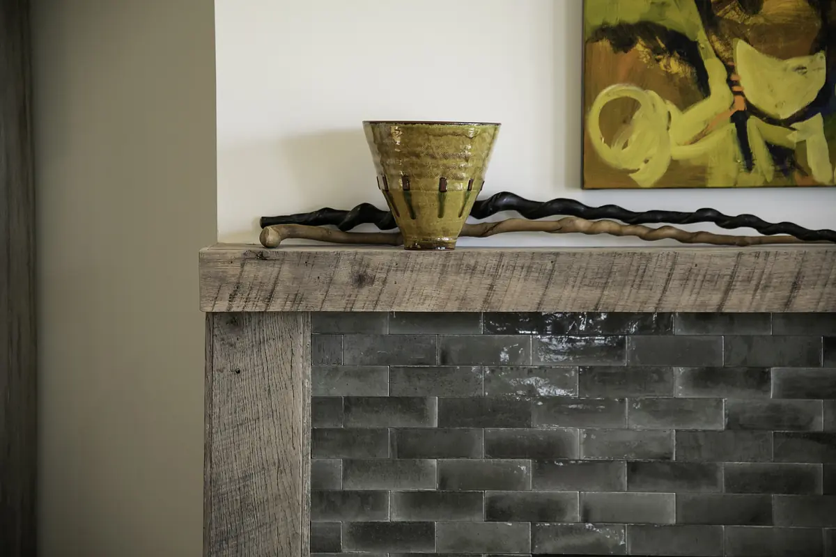 Living room with wooden mantel, ceramic pot, gray tiled wall, and abstract painting.