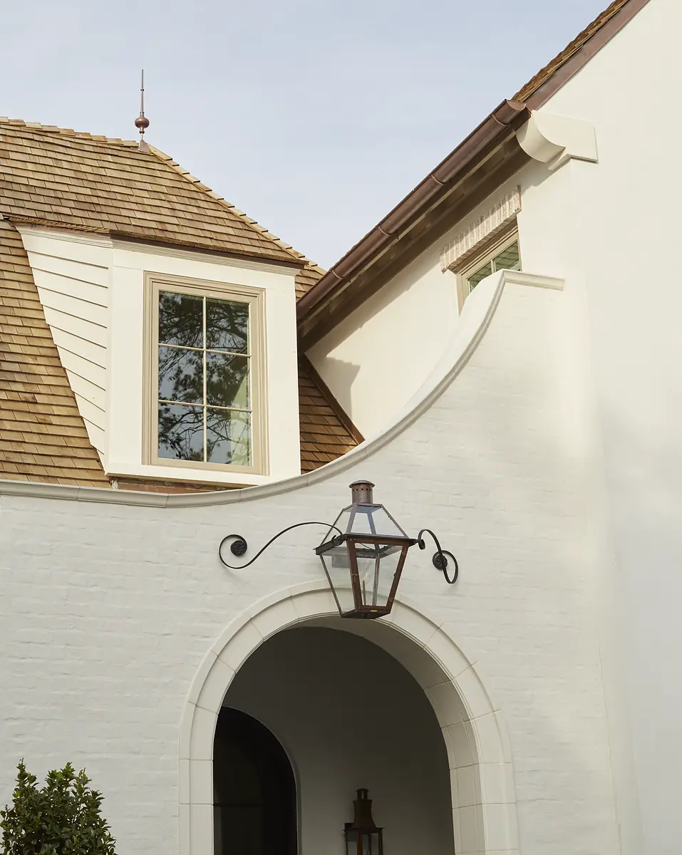 Exterior front with white brick wall, arched entrance, brown shingle roof, and mounted lantern.