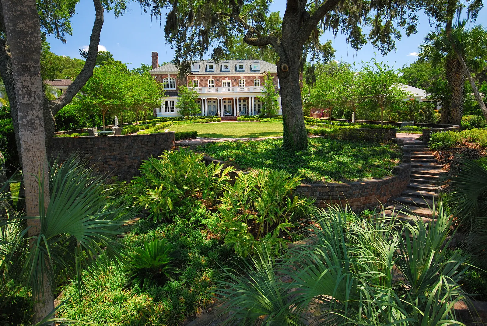 Expansive garden with lush plants, stone pathways, and a two-story brick house in the background.