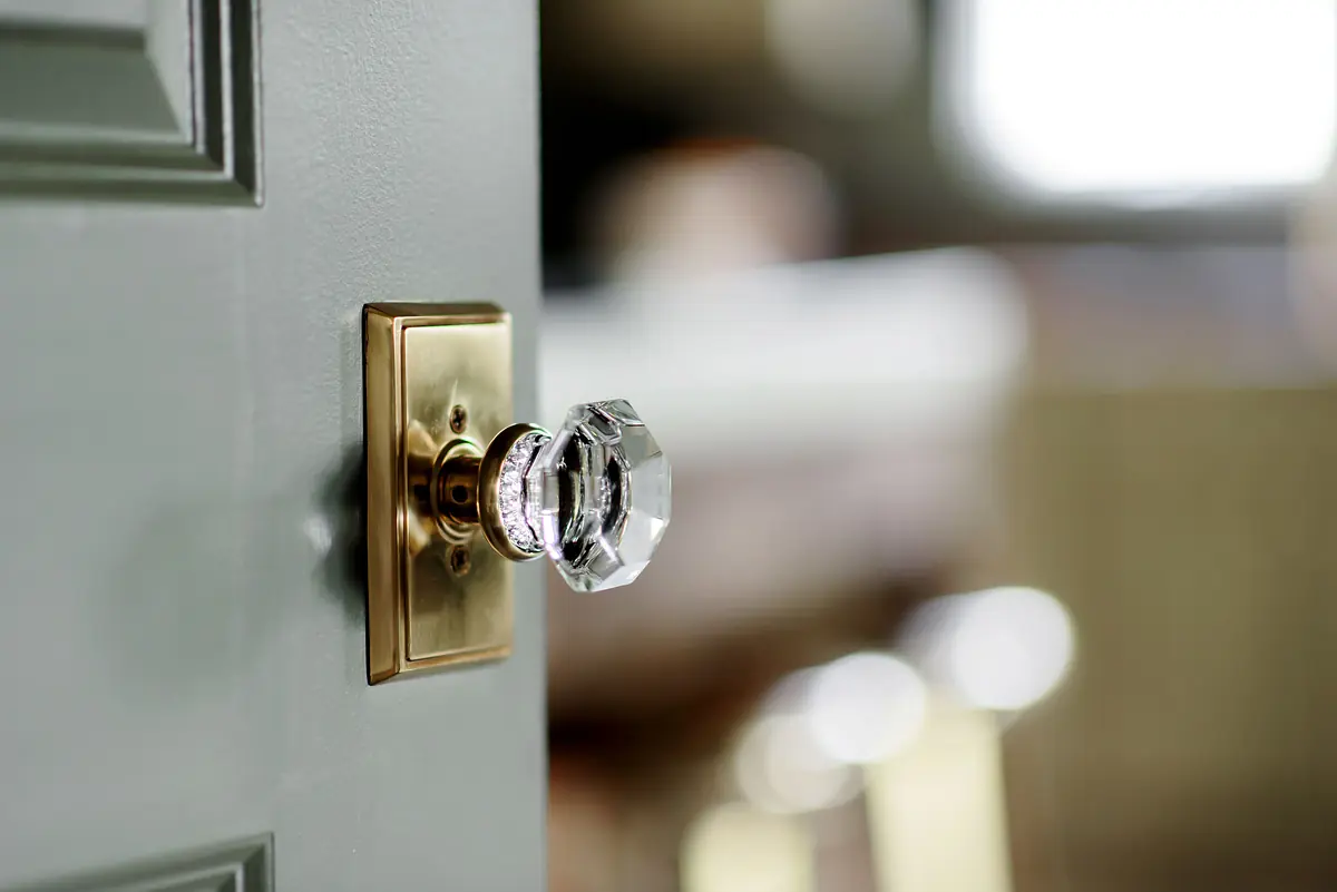 Close-up of a decorative door handle with crystal knob and brass backplate on a muted green door.