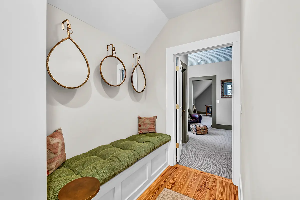 Mudroom with green bench, circular mirrors, hardwood floor, and doorway to another room.