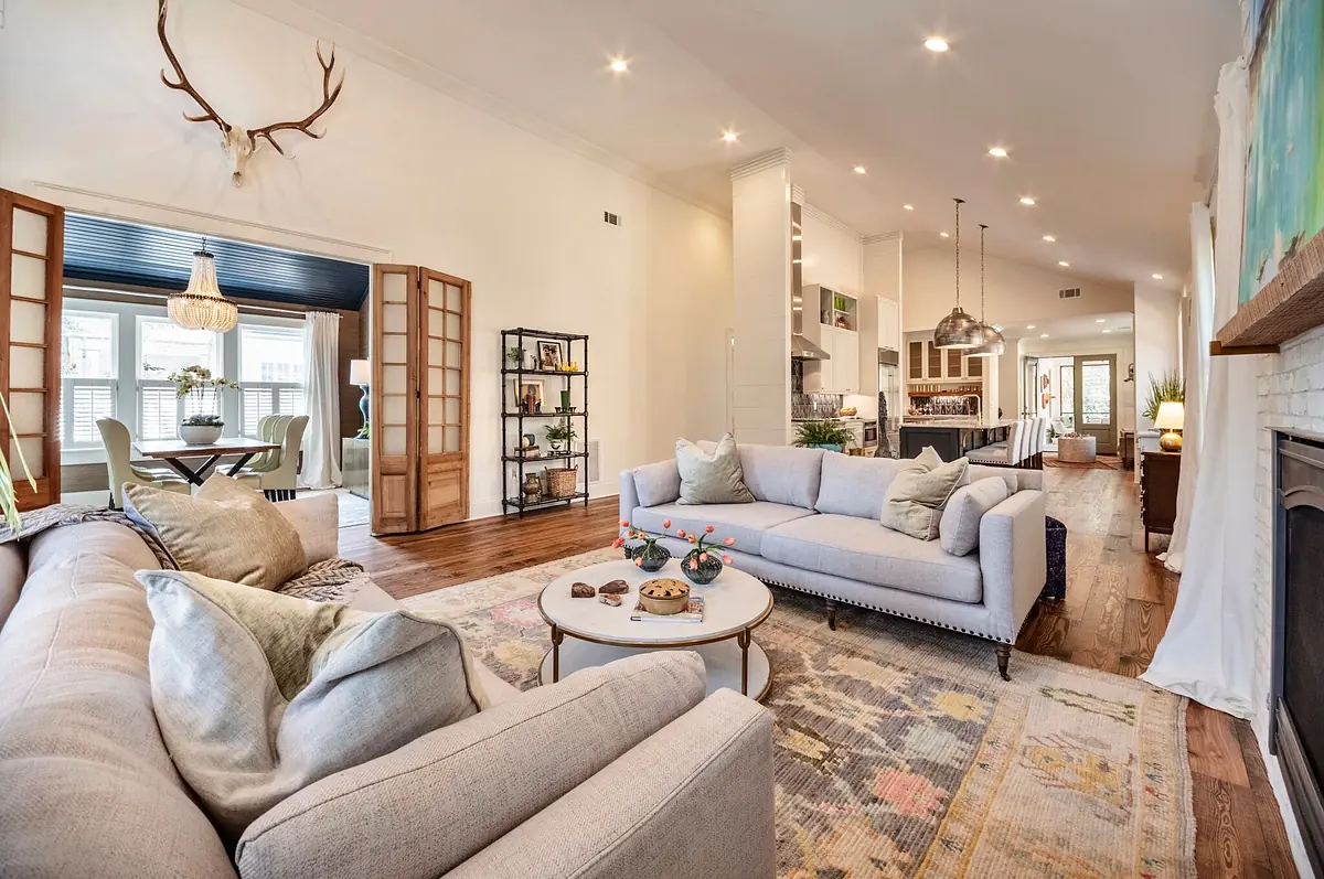 Living room with gray sectional sofa, white coffee table, area rug, bookshelves, and plants.
