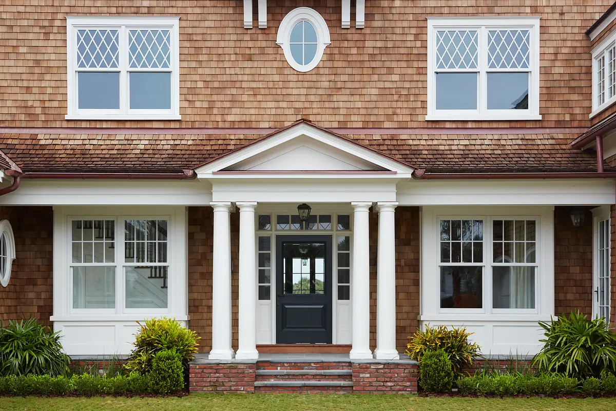 Exterior front of a house with columns, shingle walls, and landscaped plants