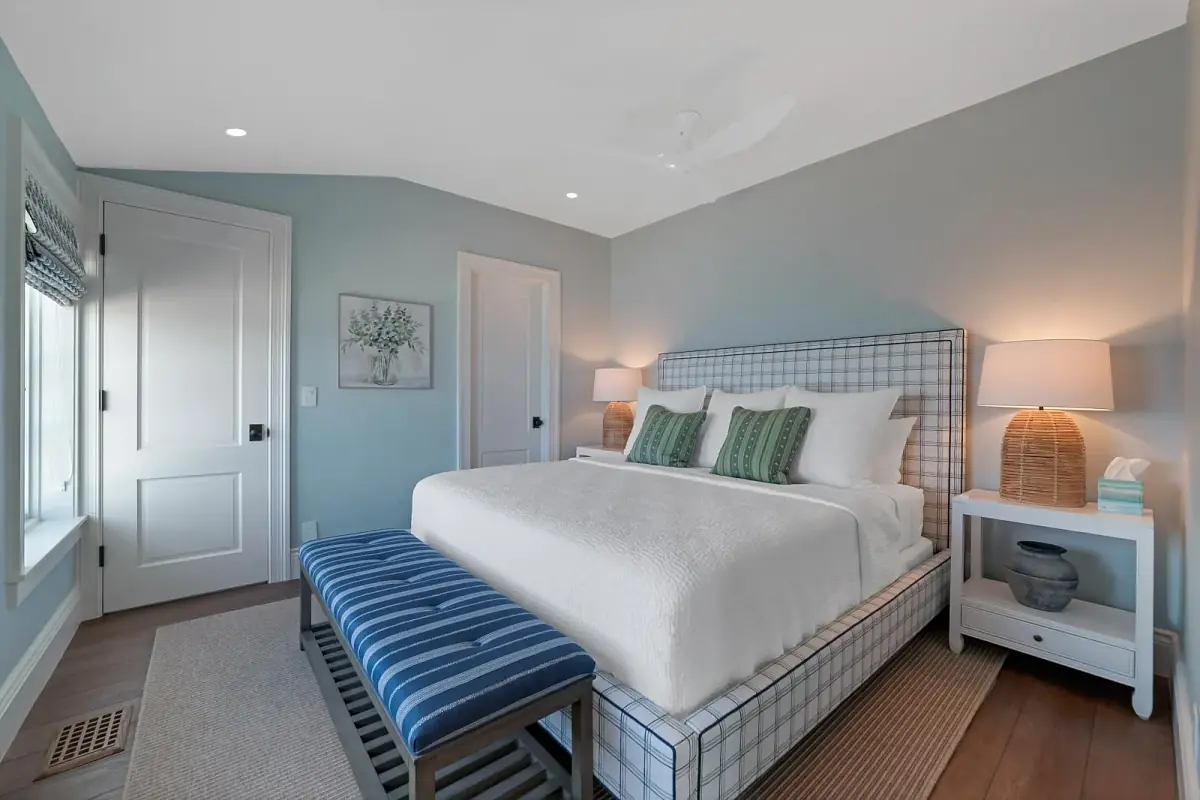 Bedroom with patterned headboard bed, white bedding, blue striped bench, nightstands, and blue walls