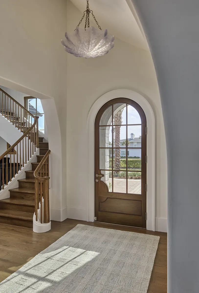 Foyer with wooden front door, cream rug, arched doorway, and curved staircase with wooden railings